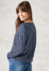 Maglietta a maniche lunghe blu navy con un motivo di foglie bianche. Tessuto morbido con scollo rotondo e vestibilità comoda, abbinata a jeans blu.