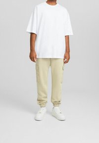 Vit oversized t-shirt med korta ärmar, kombinerad med ljusbeige cargo-joggingbyxor med sidofickor och elastiska muddar. Vita sneakers.