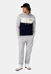 Námořnická a šedá barevně blokovaná mikina s kapucí, šňůrkami a přední kapsou, kombinovaná se světle šedými tepláky. Bílé tenisky doplňují celkový vzhled.