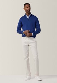 Maglione azzurro chiaro con zip, sottotaglia blu, pantaloni color crema e sneakers bianche. Trama in maglia morbida con maniche lunghe e design aderente.