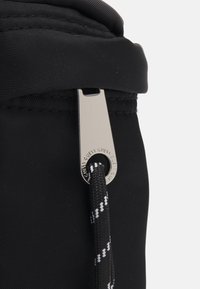 Zaino in nylon nero con cerniera metallica argento, un tirante rotondo e un accento di cordino intrecciato in bianco e nero.