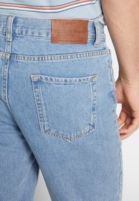Jeans in denim azzurro chiaro con un taglio classico, caratterizzati da una toppa in pelle alla vita posteriore e un design della tasca posteriore angolato.