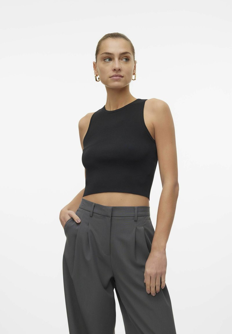 Top corto negro de canalé combinado con pantalones gris de pliegues. La tela tiene una textura suave, y el diseño cuenta con un escote alto.