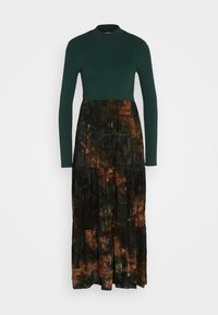 Robe à manches longues en maille côtelée vert foncé avec un col montant et une jupe noire à volants ornée de motifs abstraits orange brûlé et olive.