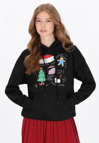 Sudadera negra con capucha que presenta gráficos coloridos con temática navideña, incluyendo un árbol de Navidad, un hombre de jengibre y regalos, con un ajuste relajado y cordones.