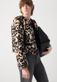 Jasje van nepbont met luipaardprint, een cropped ontwerp, zwarte accenten en een ronde halslijn, gecombineerd met donkergrijze jeans en een zwarte tas.