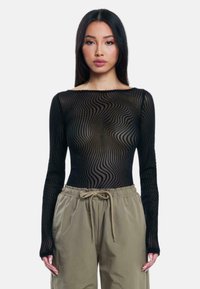 Top nero a maniche lunghe in mesh con un motivo ondulato. Il tessuto ha una texture trasparente con un collo rotondo, abbinato a pantaloni oliva con cordoncino.