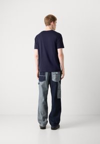 Tricou scurt cu mâneci scurte de culoare bleumarin, purtat cu pantaloni din denim cu diverse culori și croială lejeră, având mai multe buzunare în nuanțe deschise și închise.
