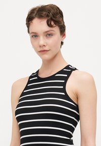 Svart- og hvitstripet tank topp med ribbet tekstur, ermene design og høy hals. Fremhevede skulderutskjæringer.