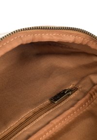 Sisäpuoli ruskeasta kangaskopasta, jolla on sileä pinta, pieni vetoketjutasku pohjalla ja kontrastivärinen ommel reunojen ympärillä.