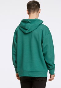 Grön hoodies av mjukt material, med avslappnad passform och långa ärmar, samt en kenguruficka och ribbade muddar.
