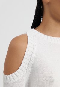 Biały dziergany top z otwartym ramieniem, prążkowanym dekoltem i teksturowanym detalem. Prosty i lekki materiał.