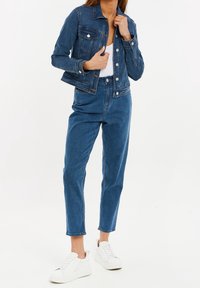 Denim jacket in dark blue with front pockets and silver buttons, paired with high-waisted dark blue jeans and white sneakers.
