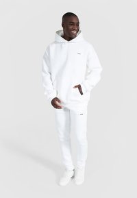 Witte hoodie met kangoeroezak en zwarte accenten, gecombineerd met witte joggingbroek en witte sneakers, met een minimalistisch ontwerp.