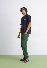 Navy short-sleeve t-shirt with orange logo, green cargo pants with pockets, and multicolored sneakers. Simple design on a plain background.