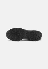 Black rubber shoe sole featuring a rugged tread pattern with deep grooves and triangular lugs for traction. Textured surface provides grip.