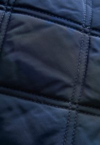 Tessuto in nylon nero trapuntato con una texture liscia, caratterizzato da linee di cucitura evidenti e una sottile lucentezza sulla superficie.