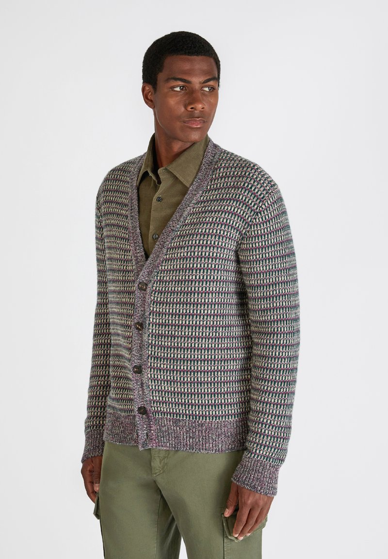 Kardigan zapinany na guziki w dzianinowym wzorze w kolorach fioletowym, zielonym i kremowym. Posiada dekolt w serek, długie rękawy oraz ściągacze na mankietach i u dołu.