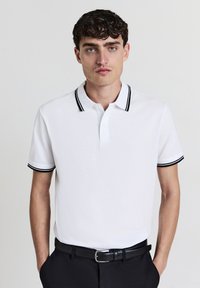 Polo bianco a maniche corte, con colletto e polsini a righe nere, dotato di pattina con tre bottoni e una texture in cotone morbida.