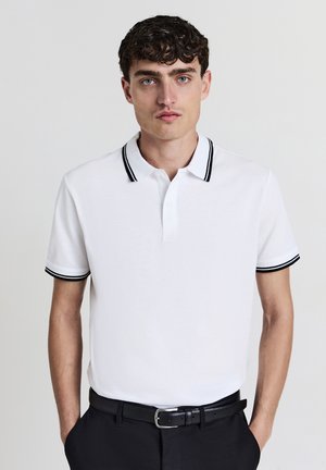 Polo blanc à manches courtes, col et poignets à rayures noires, avec une patte de boutonnage à trois boutons et une texture douce en coton.