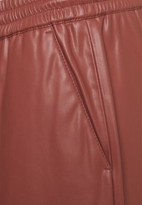 Pantalons en simili cuir marron avec une finition texturée, une taille élastique et une poche latérale avec des détails de couture soignés.
