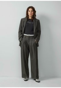 Pinstripowany ciemnozielony garnitur z dopasowanymi spodniami i czarną bluzką z krótkim rękawem. Srebrne buty dopełniają całość. Teksturowany materiał i luźny krój.