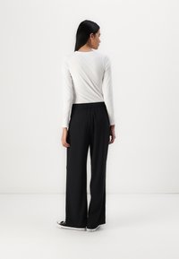 Μαύρο παντελόνι με φαρδιά πόδια και ελαστική μέση, συνδυασμένο με μια εφαρμοστή λευκή μπλούζα μακρυμάνικη. Απλός σχεδιασμός και λεία υφή υφάσματος.