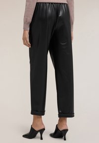 Černé kalhoty z umělé kůže s volným střihem, vysokým páskem, ohrnutými manžetami a hladkým, lesklým povrchem. Doplněny o špičaté muly.