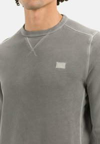 Grauer Sweatshirt mit Rundhalsausschnitt, geripptem Kragen und strukturiertem Nähten. Verfügt über ein kleines gesticktes Logo auf der Brust.