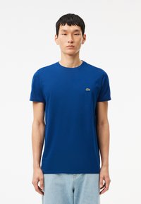 T-shirt in cotone blu con colletto a giro, maniche corte e un piccolo logo verde sul lato sinistro del petto. Design dritto.