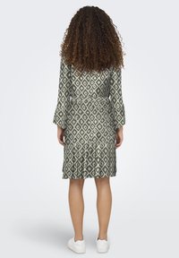 Groene jurk met een geometrisch diamantenpatroon, lange klokmouwen, een tailleband en een gerimpelde onderrand, gecombineerd met witte sneakers.