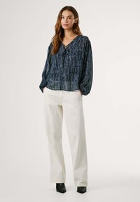 Marineblauwe blouse met lange mouwen en een V-hals, gecombineerd met witte culotte broeken en zwarte hoge laarzen. Zachte, gestructureerde stof.