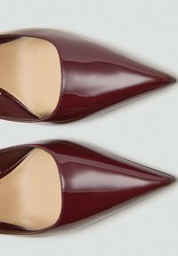 Cizme cu toc ascuțit din piele patent burgund, cu o suprafață netedă și un interior nude, având o siluetă elegantă și un design minimalist.