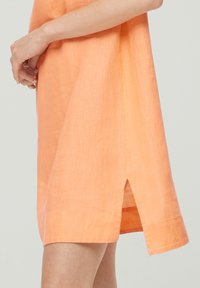 Pfirsichfarbene Leinenkleid mit lockerer Passform, seitlichem Schlitz, kurzen Ärmeln und einem strukturierten Stoff für Atmungsaktivität.