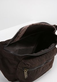 Brown fabric bag with a zippered main compartment, a textured surface, and an external zippered pocket with a metal zipper pull.