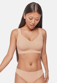 Sujetador inalámbrico nude con tirantes anchos, textura suave y diseño en V. Combinado con braguitas de bikini a juego, ambas sin costuras y minimalistas.