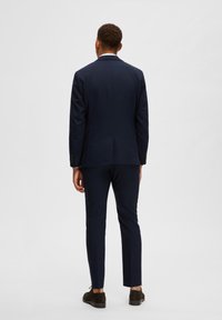 Costume marine composé d'une veste ajustée et d'un pantalon slim, fabriqué dans un tissu lisse avec une texture unie et sans motifs visibles.