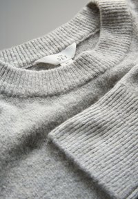 Maglione grigio chiaro con corpo strutturato e collo a costine. L'etichetta indica la taglia media. Materiale morbido con una finitura pulita.