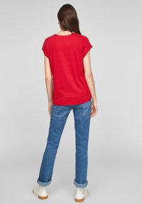 Rød kortærmet t-shirt med rund halsudskæring, kombineret med blå jeans i denim, opkørte buksekanter og hvide ankelstøvler med brune såler.