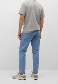 Maglietta a maniche corte grigio chiaro, jeans di jeans blu e sneakers beige. I jeans hanno una vestibilità comoda e dettagli di cuciture visibili.