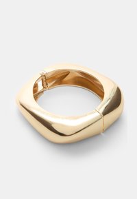 Bracciale in metallo dorato con un design liscio e scolpito; presenta una cerniera a molla per una facile indossabilità e una forma leggermente arrotondata.