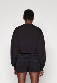 Svart kort sweatshirt med ribbad krage, långa ärmar och elastisk fåll, kombinerad med fransade svarta denimshorts med bakfickor.