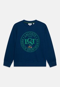 Sudadera azul marino de tejido suave con un gráfico circular verde que incluye el texto "LACOSTE PARIS FRENCH SPORTSWEAR" y un logo de cocodrilo.