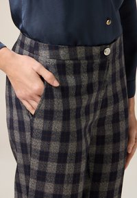 Spodnie w kratkę wykonane z teksturowanej tkaniny w odcieniach szarości, granatu i brązu. Widoczna kieszeń boczna z ozdobnym srebrnym guzikiem.