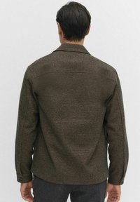 Bruine geweven jas met een kraag, textuurstof, lange mouwen en knoopmanchetten. Heeft een rechte snit en een eenvoudig ontwerp aan de achterkant.