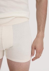 White cotton boxer shorts with a soft, ribbed texture, featuring an elastic waistband, showcased against a neutral background.
