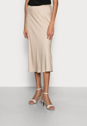 Jupe midi beige avec une texture lisse et une légère évasement à l'ourlet, associée à des sandales blanches à talons hauts à brides.