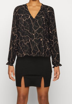 Kobieta ubrana w czarną bluzkę z dekoltem w serek z beżowymi, abstrakcyjnymi liniami oraz czarną mini spódnicę z dwoma przednimi rozcięciami.