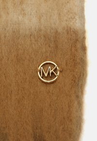 Matériau en feutre marron avec un accent rond du logo MK en ton or. La texture est douce avec une légère peluche, accentuant un aspect moelleux.