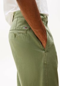 Pantaloni in cotone verde oliva con una tasca laterale e una tasca posteriore con bottone. Piccolo logo del marchio sulla tasca posteriore.